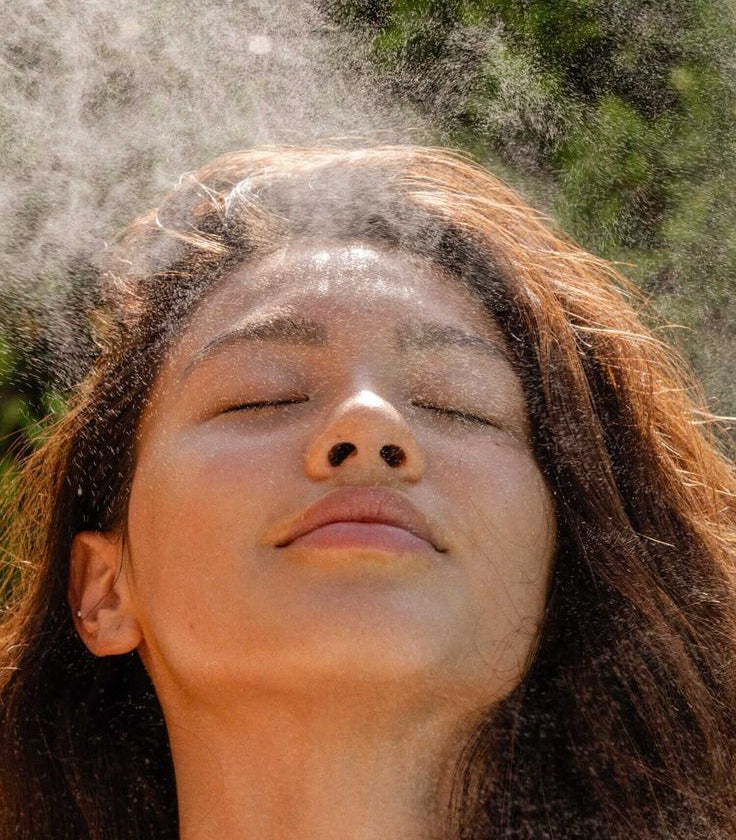 Person with water droplets on their face against a natural background